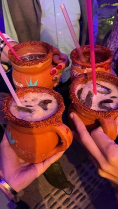 three people holding up orange cups with drinks in them and straws sticking out of them