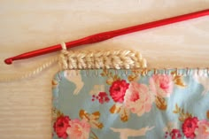 a red crochet hook is next to a piece of fabric with flowers on it