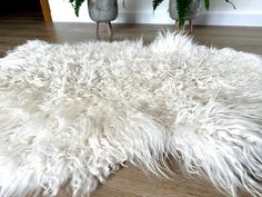 a white shaggy rug is on the floor in front of two potted plantes