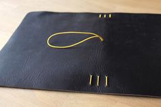 a black leather notebook with yellow pins on it sitting on top of a wooden table