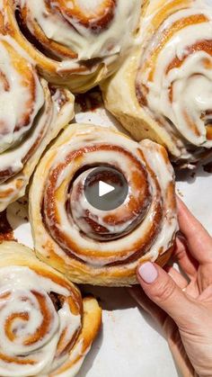 cinnamon rolls with icing sitting on top of a white plate next to a person's hand