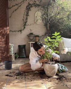 a woman kneeling down next to a potted plant with dirt on the ground in front of her