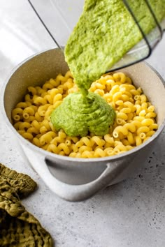 a bowl filled with macaroni and pesto being stirred by a hand mixer