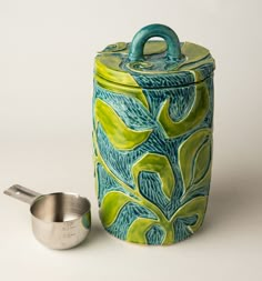 a green and blue ceramic container next to a measuring cup on a white tablecloth