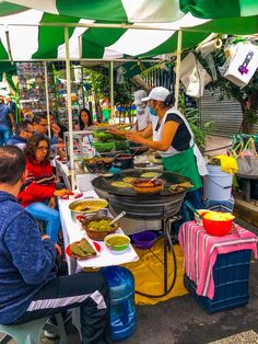 people sitting at tables with food on them under umbrellas in an open air market