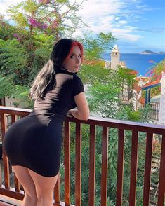 a woman with red hair is standing on a balcony looking out at the ocean and trees