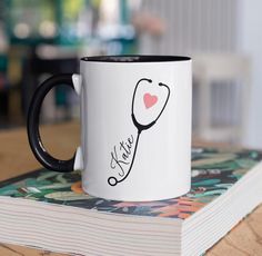 a black and white coffee mug with a stethoscope on it sitting on top of a book