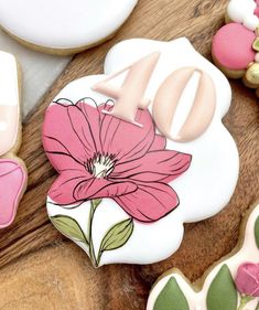 decorated cookies with pink flowers and green leaves on a wooden table next to cookie cutters