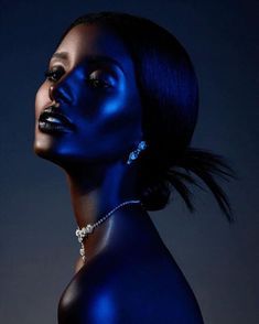 a woman with blue paint on her face and neck, posing for the camera in front of a dark background