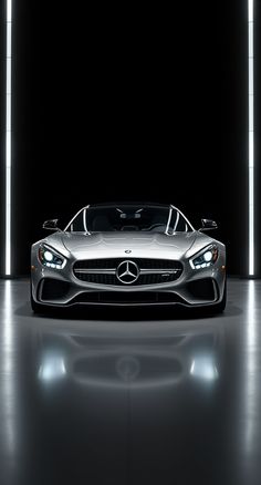 the front end of a silver mercedes sports car in a dark room with lights on