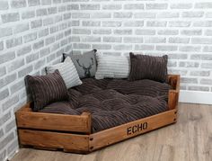 a couch made out of wooden pallets with pillows on the top and bottom, sitting in front of a brick wall