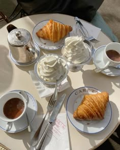 there is a croissant, coffee and cream on the table with other food