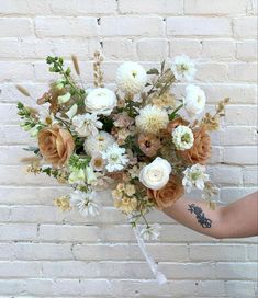 a person holding a bouquet of flowers against a brick wall