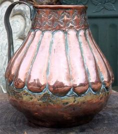 a copper colored pitcher sitting on top of a wooden table next to a green door