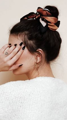 a woman with her hands on her face, wearing black nail polish and a bow in her hair