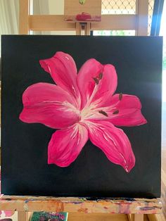 a pink flower painted on a black canvas in front of a table with other art supplies