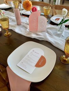 the table is set with pink and white plates, napkins, and place cards