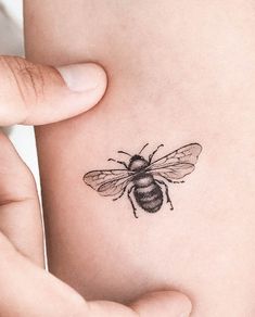 a small bee tattoo on the back of a woman's left arm is shown