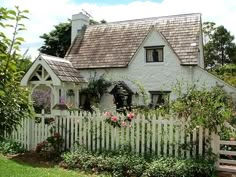 a white picket fence in front of a house with purple flowers on the window sill