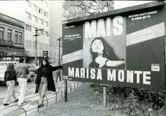 a woman standing next to a large sign on the side of a road with her arms outstretched