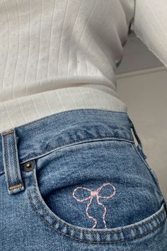 the back of a woman's jean pants with an embroidered pink bow on it