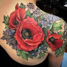 a woman's back with flowers and leaves painted on her shoulder, which is covered in tattoos