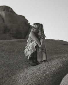 a woman sitting on top of a rock next to a mountain