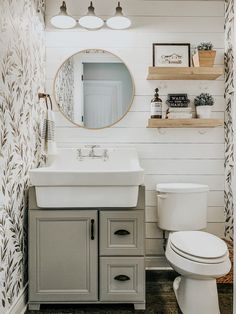 a white toilet sitting next to a sink in a bathroom under a mirror and shelves