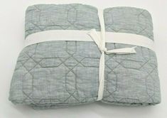 a gray quilted blanket with a white ribbon tied around the edge on a white background