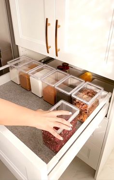 a person reaching for food in an open drawer on a kitchen counter with white cabinets