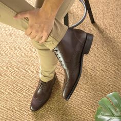 a man is sitting on a chair with his foot in the air and wearing brown shoes