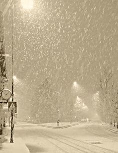 a clock on a pole in the middle of a snow covered street with trees and lights