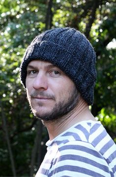 a man in striped shirt and hat holding a cell phone up to his ear with trees in the background