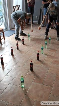 a group of people standing in a room with bottles on the floor and one person holding a baseball bat