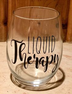 a wine glass with the words liquid therapy written in cursive writing on it