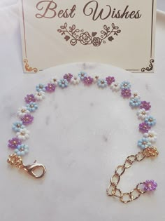 a bracelet with blue and purple flowers on it next to a sign that says best wishes