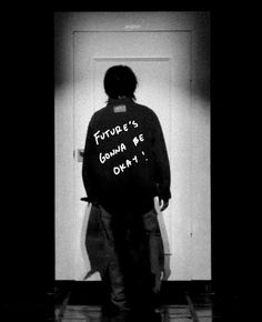 a man standing in front of a white door with writing on the back of his jacket