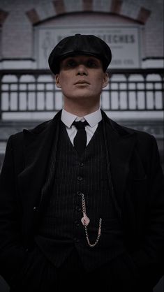 a man wearing a suit and tie with a hat on his head is standing in front of a building