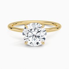 a yellow gold engagement ring with a round cut diamond in the center, on a white background