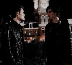 two young men standing next to each other in front of a clock tower at night