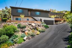 a large house sitting on the side of a road next to a lush green hillside