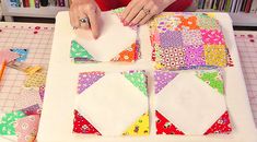 a woman is making a quilt on a table with scissors and paper pieces in front of her