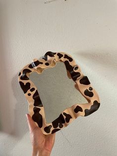 a hand holding up a mirror that is shaped to look like a cow print pattern