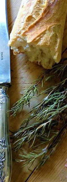 a knife sitting on top of a cutting board next to some bread and sprigs