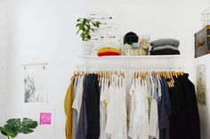 a white closet with clothes hanging on racks and plants in the corner next to it