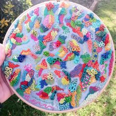 someone is holding up a colorful embroidery project in their hand and it looks like they are made out of buttons