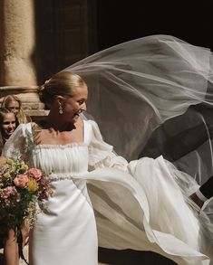 a woman in a white wedding dress and veil walking with her bridesmaids behind her