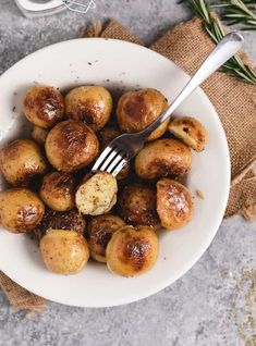 a white bowl filled with cooked potatoes on top of a table next to a fork