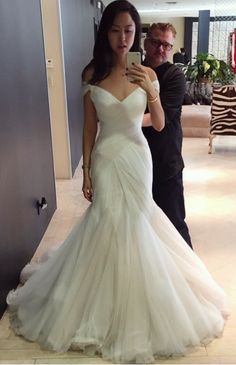 a woman in a wedding dress taking a selfie with her cell phone while standing next to a man