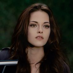 a woman with long brown hair standing in front of a car looking at the camera